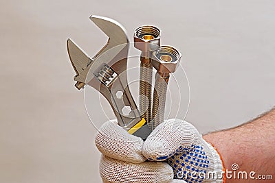 Plumber hand holding adjustable wrench and flexible tubes Stock Photo