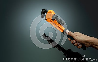 Plumber hand holding handle of chrome pipe wrench isolated on dark background. Metal monkey wrench for plumber. Mechanic tools. Stock Photo