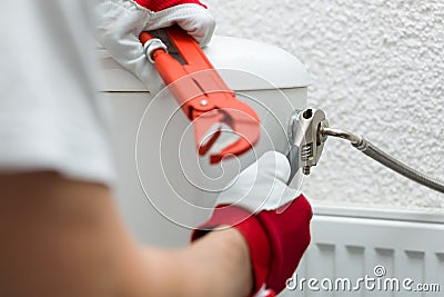 Plumber installing pipe to water closet with wrench Stock Photo