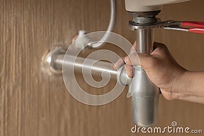 Plumber repairs and maintains chrome siphon under the washbasin in bathroom. Stock Photo