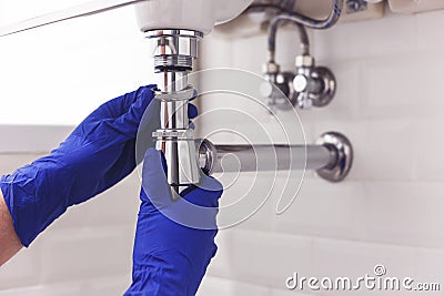 Plumber repairs and maintains chrome siphon under the washbasin. Plumber at work in bathroom, plumbing assemble and Stock Photo