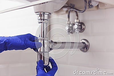 Plumber repairs and maintains chrome siphon under the washbasin. Plumber at work in bathroom, plumbing assemble and Stock Photo