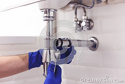 Plumber repairs and maintains chrome siphon under the washbasin. Plumber at work in bathroom, plumbing assemble and Stock Photo