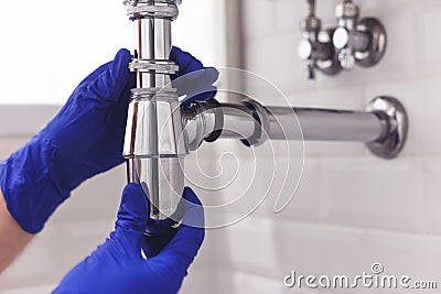 Plumber repairs and maintains chrome siphon under the washbasin. Plumber at work in bathroom, plumbing assemble and Stock Photo