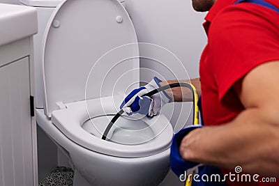 Plumber unclogging blocked toilet with hydro jetting at home bathroom. sewer cleaning service Stock Photo