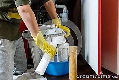 Plumber in yellow household gloves changes water filters. Repairman installing water filter cartridges in kitchen. Stock Photo