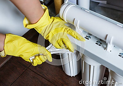 Plumber in yellow household gloves changes water filters. Repairman installing water filter cartridges in kitchen. Drinkable water Stock Photo