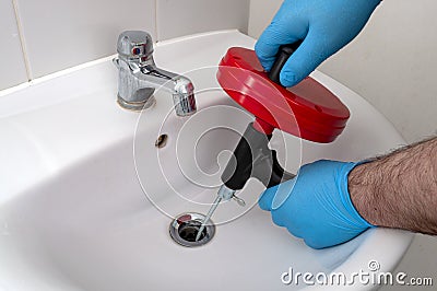 Plumbing issues, occupation in sanitation and handyman contractor concept with plumber repairing drain with plumbers snake steel Stock Photo