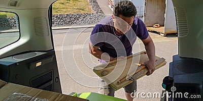 Caucasian man unloads wooden planks from car trunk to station of collection of large-size garbage on spring sunny day Stock Photo