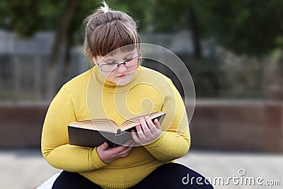 Plump girl in glasses sits alone in park and reading book Stock Photo