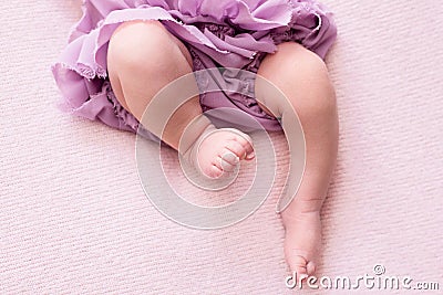 Plump legs of a newborn girl in a lilac skirt, young ballerina dancer, fingers on her feet, dance moves, pink background, Stock Photo