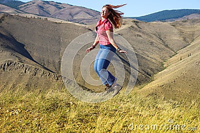 Plump white haired caucasian girl in jeans and hiking boots jumping on the field Stock Photo