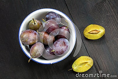 Plums in a bowl, whole and halved on dark brown wood Stock Photo
