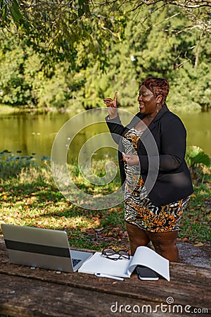 Plus size CEO businesswoman boss giving a speech in an online group meeting. She is working remotely in the park Stock Photo