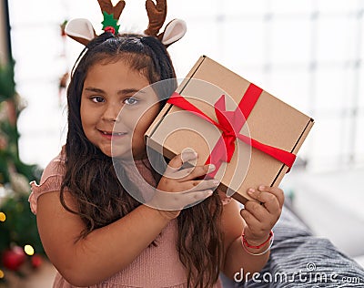 Plus size hispanic girl hearing gift sound standing by christmas tree at home Stock Photo