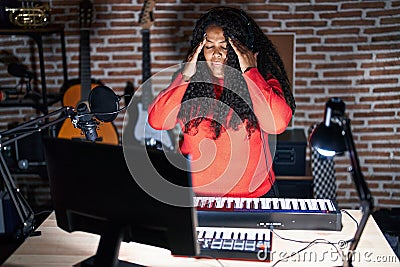 Plus size hispanic woman playing piano at music studio with hand on head for pain in head because stress Stock Photo