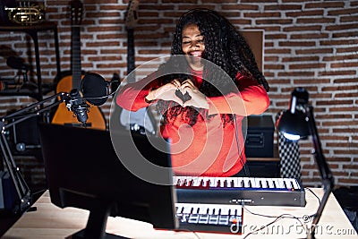 Plus size hispanic woman playing piano at music studio smiling in love doing heart symbol shape with hands Stock Photo