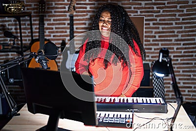 Plus size hispanic woman playing piano at music studio winking looking at the camera with sexy expression, cheerful and happy face Stock Photo