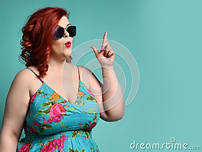 Plus-size overweight lady in sunglasses and sundress point her finger up like she has got an idea at free text copy space on mint Stock Photo