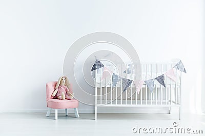 Plush toy on pink chair next to white crib in white baby`s bedro Stock Photo