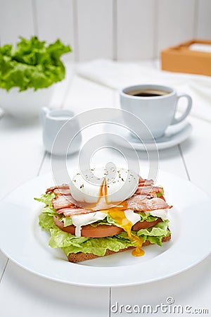Poached egg sandwich with bacon, salad, mayonnaise, tomatoes, toasted bread Stock Photo