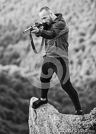 Poaching concept. Poacher stand on edge of cliff. Hunter poacher looking for victim. Hunter with rifle nature Stock Photo