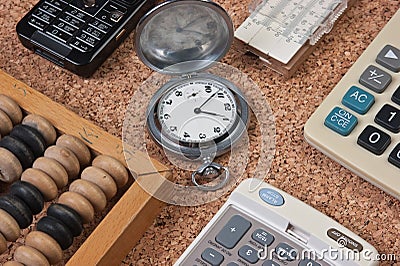 pocket watch, a calculator, a wooden abacus on a cork board Stock Photo