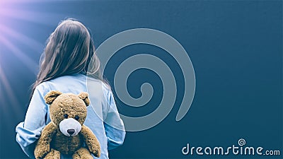a girl looking at a gloomy wall with a teddy bear at her back trying to cope with her mental illness Stock Photo