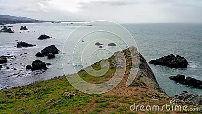 Cliffs edge pointing dangerously over rocky ocean shore Stock Photo