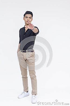 A poised young Filipino man wearing casual attire sternly gestures with a stop hand signal against a white backdrop Stock Photo