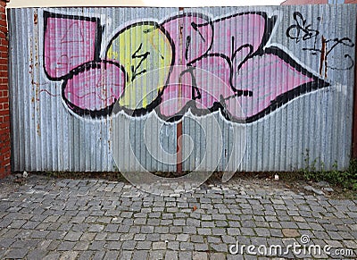 Two color graffiti on an old metal gate in front of which paving stones. Editorial Stock Photo