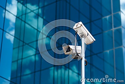 Pole with two white video surveillance cameras at big office glass building background Stock Photo