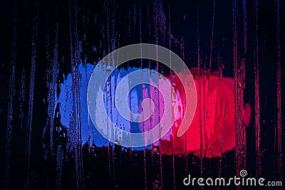 An abstract background of police lights bokeh trough wet glass at night close-up with selective focus Stock Photo