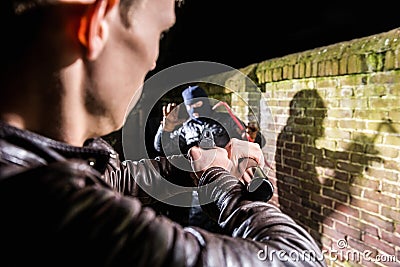 Police officer aiming torch and gun towards busted scared burgla Stock Photo