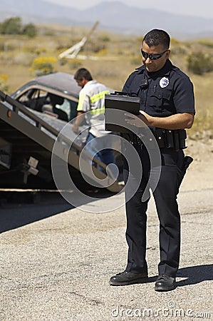 Police Officer Writing Notes At Car Crash Scene Stock Photo