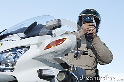 Policeman Monitoring Speed Through Radar Against Sky Stock Photo