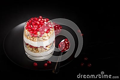 Pomegranate parfait - sweet organic layered dessert with granola flakes, yogurt and fruit seeds on black background. Stock Photo