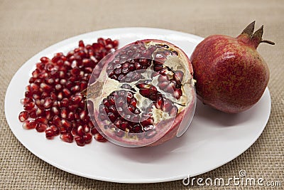 Pomegranates have broken into pieces with red berries on a porcelain plate on a textile background. Stock Photo
