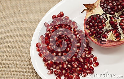 Pomegranates have broken into pieces with red berries on a porcelain plate on a textile background. Stock Photo