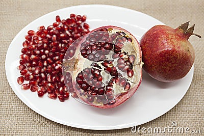 Pomegranates have broken into pieces with red berries on a porcelain plate on a textile background. Stock Photo