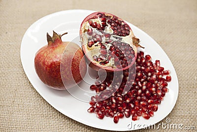 Pomegranates have broken into pieces with red berries on a porcelain plate on a textile background. Stock Photo