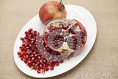 Pomegranates have broken into pieces with red berries on a porcelain plate on a textile background. Stock Photo