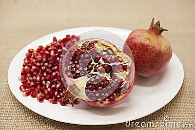 Pomegranates have broken into pieces with red berries on a porcelain plate on a textile background. Stock Photo