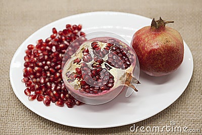 Pomegranates have broken into pieces with red berries on a porcelain plate on a textile background. Stock Photo