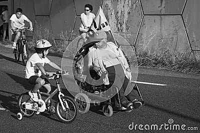 Boy on a bicycle looks curiously at a man in a wheelchair. Editorial Stock Photo