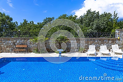 Pool with blue water ladder for descent and ascent into the water. The sun loungers are empty by the pool Stock Photo
