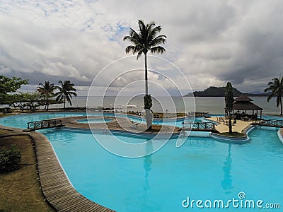 A pool at a resort with a palmtree on center and the ocean as background,Ilheu das Rolas,Sao Tome Stock Photo