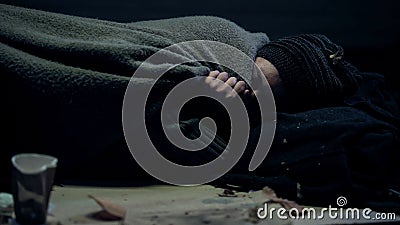 Poor beggar covered dirty blanket sleeping on street feeling cold, homelessness Stock Photo