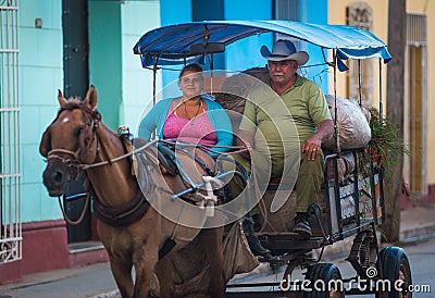 Poor Cuban couple in traditional colorful alley with traditional carriage, in old Trinidad, Cuba, America. Editorial Stock Photo