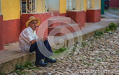 Poor Cuban senior man in traditional colorful alley with colonial house, in old town, Cuba, America. Editorial Stock Photo